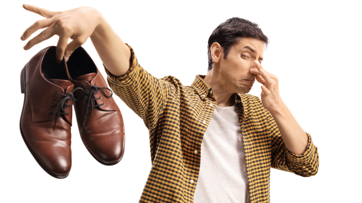 Hombre tapándose la nariz mientras sostiene un par de zapatos.