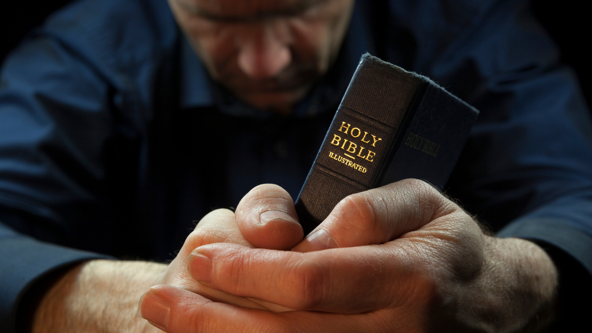 Hombre orando con Biblia en sus manos (Getty Images)